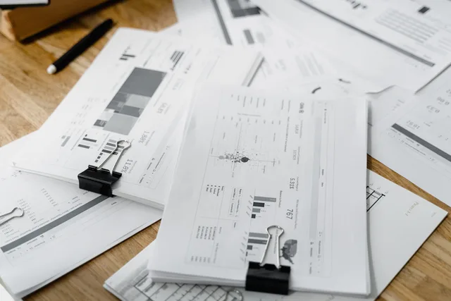 A stack of financial reports and graphs with clips on a wooden desk, highlighting business planning. Sådan læser du koncernstrukturer i årsrapporter