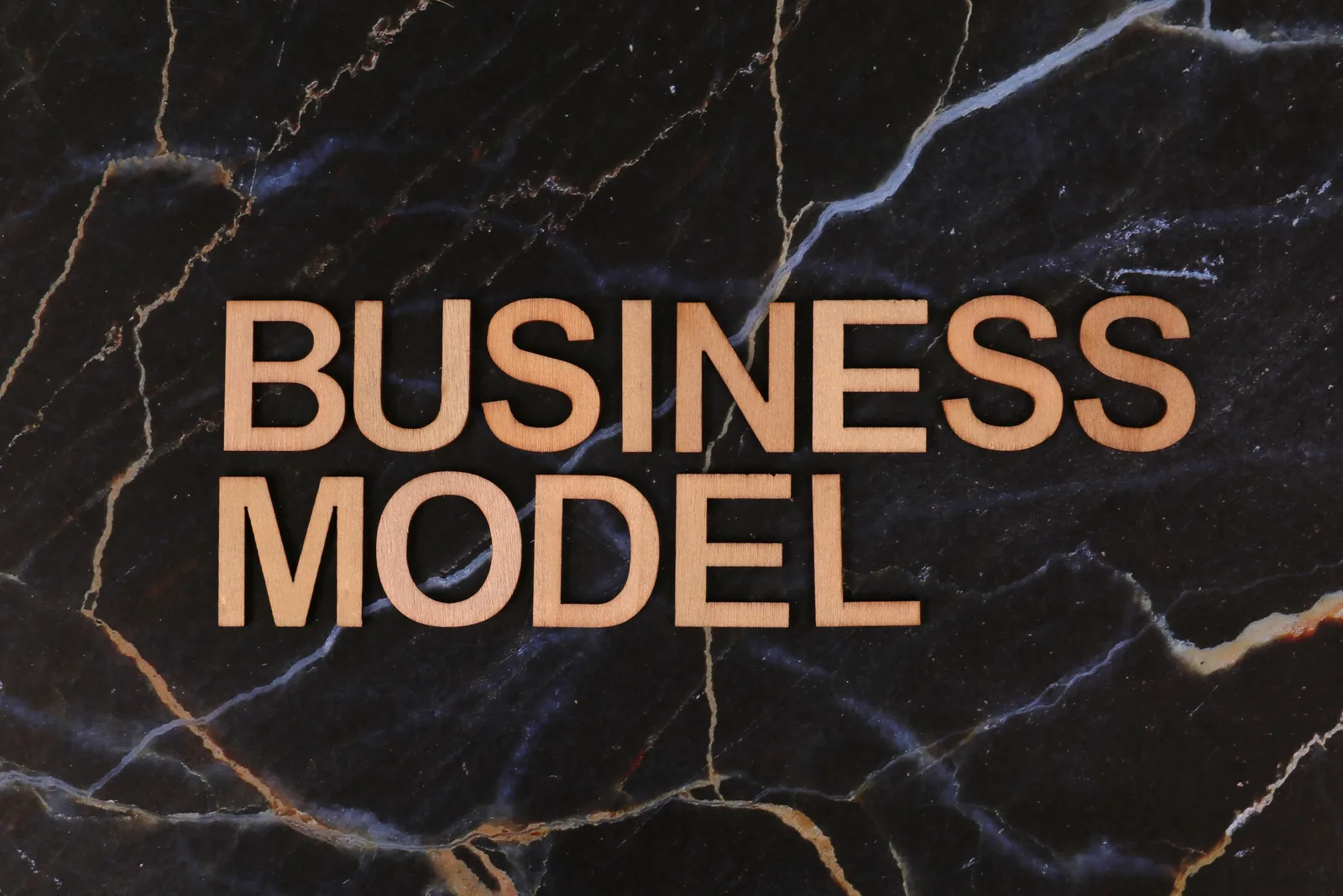 Wooden letters spelling 'BUSINESS MODEL' on a dark marble background.